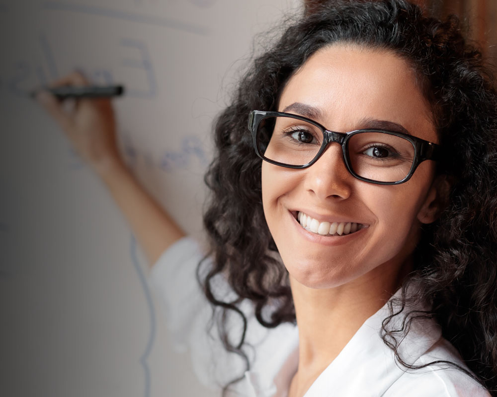 female teacher with glasses smiling whislt writing on a whiteboard